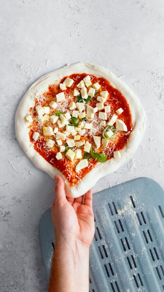 A hand preparing fresh homemade pizza with cheese and basil. Perfect for gourmet culinary projects.