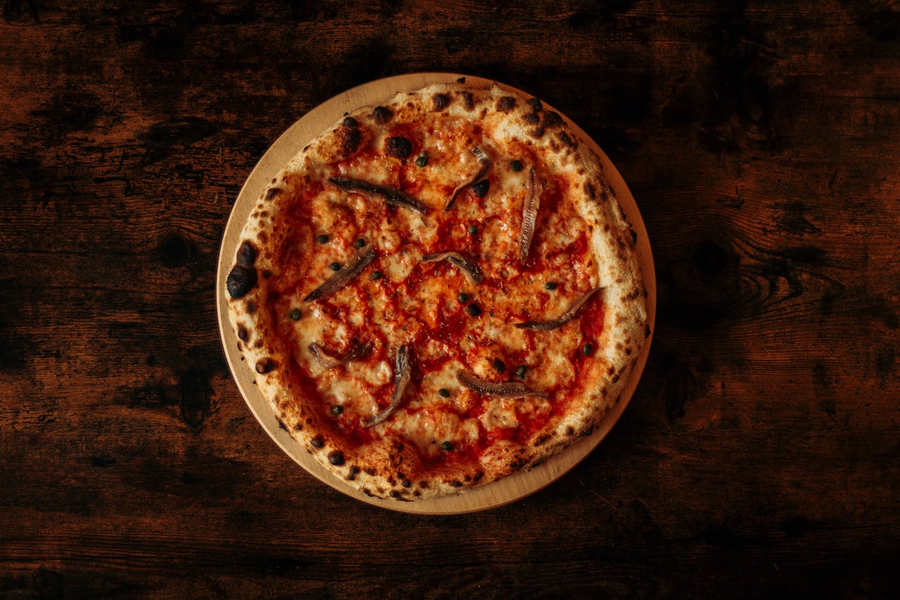 Top view of a pizza with anchovies, tomato sauce, and cheese on a rustic wooden table.