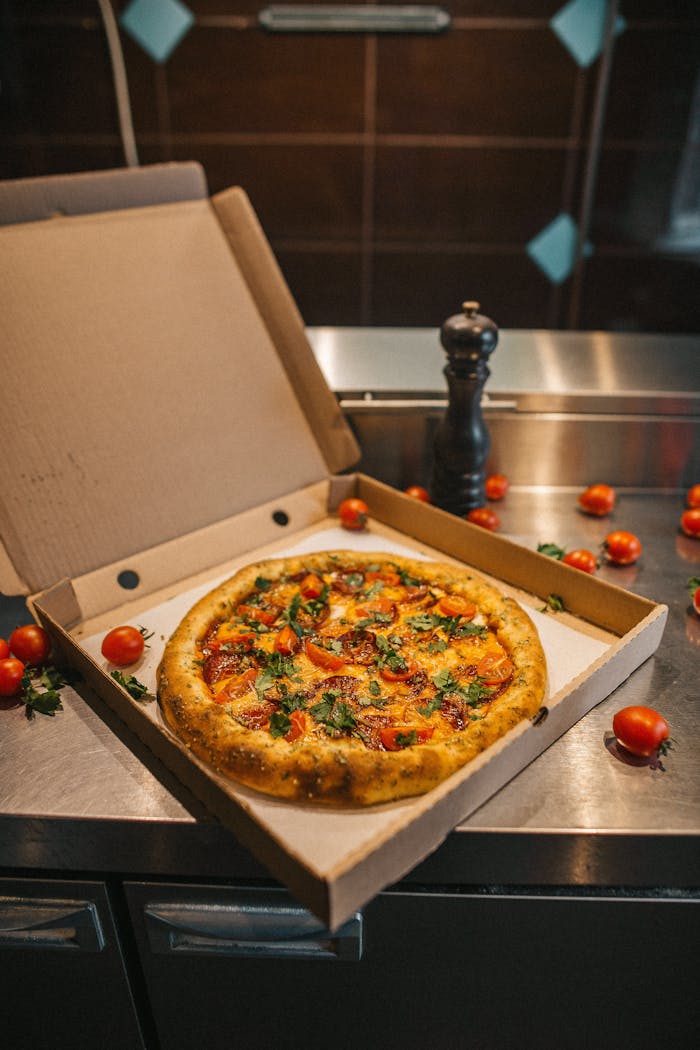 A mouth-watering pizza with fresh tomatoes and herbs in an open box on a kitchen counter.